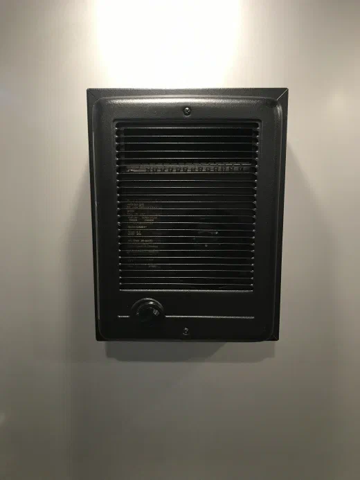 Thermostat-controlled electric wall heater mounted inside a restroom trailer